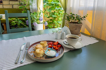 Delicious breakfast with syrniki (cottage cheese pancakes), fresh strawberries, and coffee on summer terrace.A beautiful morning meal with sour cream, almonds, berries, and coffee in garden cafe