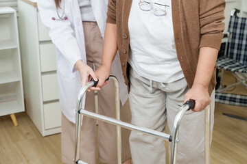 Close up of elderly asian woman gripping walker handles with orthopedic doctor nearby assisting...