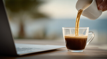 Hand pours coffee with golden light filtering in, laptop and notes softly blurred