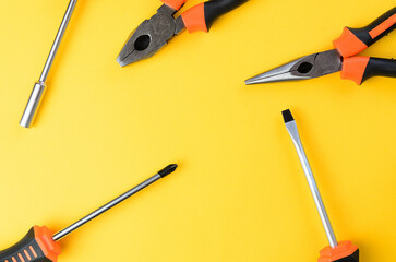 Empty yellow background with flathead philips screwdriver and pliers sides top view