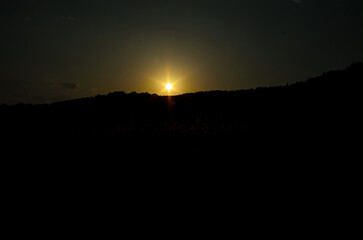 Sunset with bright glowing sun rays dark silhouette landscape little sky dramatic scene evening