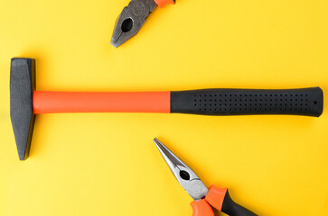 Hammer centered with cropped pliers on both sides on bright yellow background top view