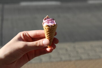 Hand holding colorful ice cream cone with pink topping against neutral background showcasing summer...