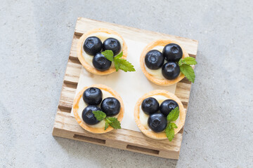 Mini round tartlet with blueberries and mint. On a wooden board. Light grey background. Top view
