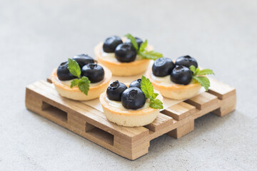 Mini round tartlet with blueberries and mint. On a wooden board. Light grey background