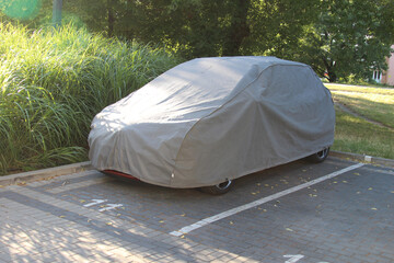 Silver car covered with protective tarp parked on residential street surrounded by green vegetation