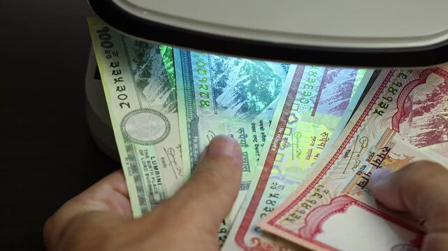 Examination of nepalese rupee (NPR) cash money with UV counterfeit detector. Concept of authenticity check, fight against counterfeiting of banknotes, anti fraud measures in Nepal. Close up view.
