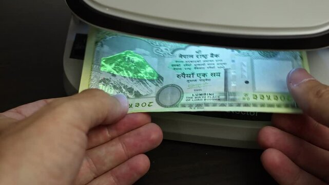 Examination of nepalese rupee (NPR) cash money with UV counterfeit detector. Concept of authenticity check, fight against counterfeiting of banknotes, anti fraud measures in Nepal. Close up view.