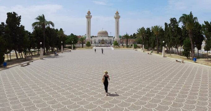 Panoramic aerial view of the Mausoleum of Habib Bourguiba located in Monastir, Tunisia with stylish tourist woman with hat sightseeing a patterned square