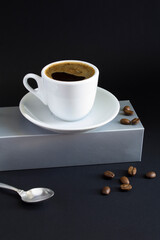 Black coffee in the white cup that stands on a gray podium on a black background.