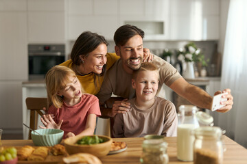 Happy family having fun while taking a selfie during breakfast in dining room