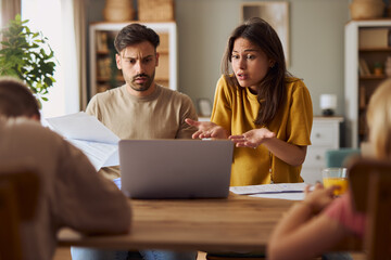Frustrated parents talking about financial bills during e-banking over a computer at home.