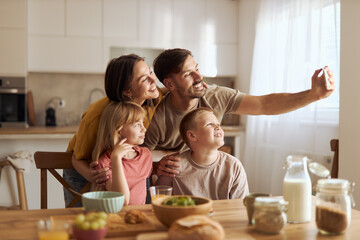 Happy family having fun while taking a selfie during breakfast in dining room
