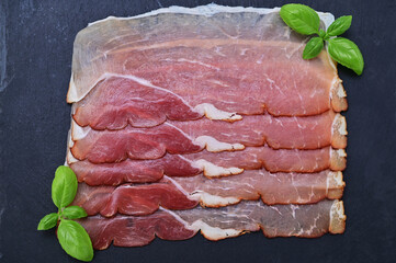 sliced ​​smoked ham on a black board and basil leaves