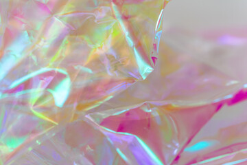 Close-up of iridescent crinkled cellophane foil with vibrant reflections in pink, yellow, green,...
