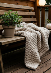 Fototapeta premium Cozy knitted blanket and green plant on a rustic wooden bench outdoors