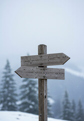 Naklejka premium Wooden directional signpost in a snowy winter landscape with blurred pine trees