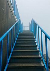 Outdoor concrete stairs with bright blue railings disappear into the thick fog