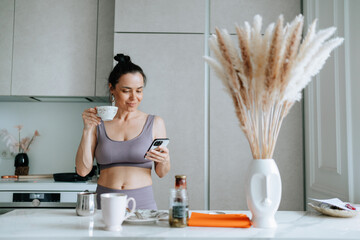 A woman enjoys a relaxed morning, sipping coffee and checking her phone, epitomizing laid-back lifestyle amidst a chic kitchen setting.