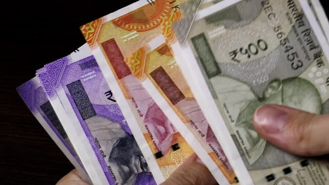 Close up view of woman's hands counting Indian currency notes (INR). Indian cash money of 500, 200 and 100 rupees denominations. Real time motion video.	