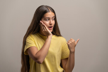 Surprised young woman gossiping and pointing with her thumb.
