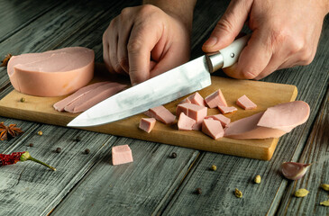 Hands skillfully slice deli meat on a wooden cutting board. Various diced pieces lay scattered as...