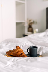 Cozy hotel room with breakfast, featuring a croissant and a cup of coffee