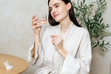 Woman taking vitamin pill with glass of water in a serene indoor setting