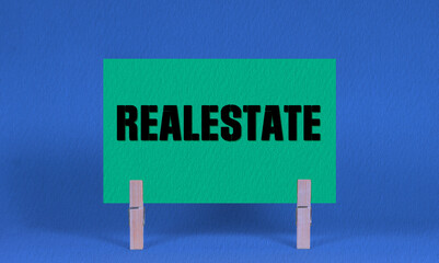REALESTATE Symbol. Concept words REALESTATE on Green Rectangle Paper Held by Wooden Clothespin Blue...