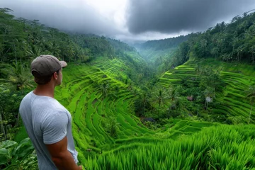 Fototapete View of lush rice terraces in Bali during cloudy weather with a man admiring the landscape © YouraPechkin