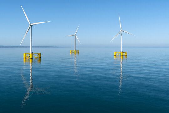 A wide view of Kincardine WindFloat units on a calm sea, with the faint outline of the Aberdeen coast in the distance, floating offshore wind-turbines