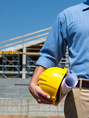 Construction worker holding yellow hard hat and blueprints at building site