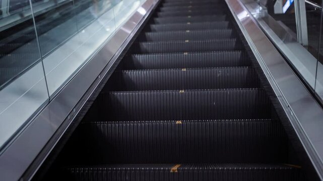 Long escalator moving upward, filmed from overhead in a symmetrical layout with metallic handrails and subdued lighting during a quiet moment without people.