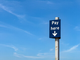 Pay Here sign in a car park isolated against a blue sky. No people.