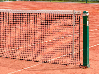Close up view of part of the net on a clay tennis court. No people.