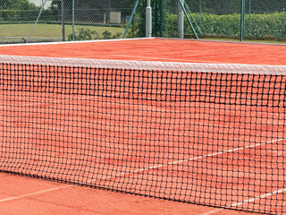 Close up view of part of the net on a clay tennis court. No people.