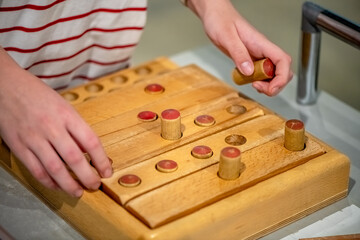 Close-up of a child's hands manipulating wooden pieces on an educational toy, engaging in a playful activity that enhances fine motor skills and problem-solving abilities