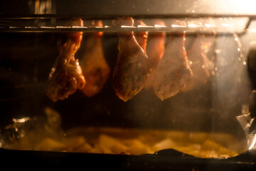Chicken drumsticks roasting in an oven, dripping juices onto a tray below. The warm glow highlights...
