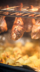 Chicken drumsticks roasting in an oven, dripping juices onto a tray below. The warm glow highlights the crispy texture, creating an appetizing and savory scene