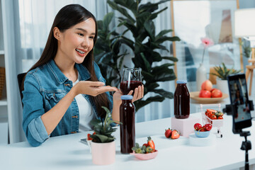 Smiling young beautiful Asian reviewing tasty mixed strawberry and cherry juice detox drinks, showing healthy product to promote for special promotion selling on social media online record. Stratagem.