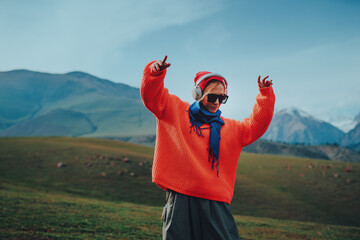 Young stylish woman in orange sweater dancing in the mountains