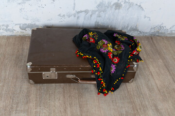 Vintage old classic travel leather suitcase circa 1940-60s with a vintage scarf. Travel luggage concept. Retro brown suitcase on a white wall background.