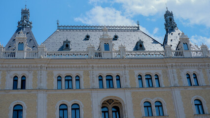 A detailed view of a grand building’s facade, with intricate architectural elements and decorative windows under a blue sky.