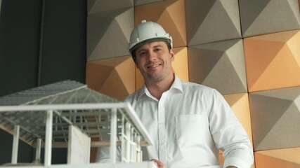 Closeup of smiling confident architect engineer wearing safety helmet while standing with arms folded with house model placed on table. Creative business living and design concept. Manipulator. - Powered by Adobe