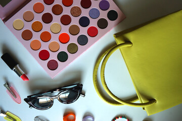 Green bag, various colorful jewelry, sunglasses, hair accessories and colorful make up on white background. Flat lay.