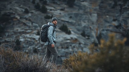 A man treks through the mountain wilderness, wearing a backpack and winter hat, ready for outdoor adventure and exploration on the trail.