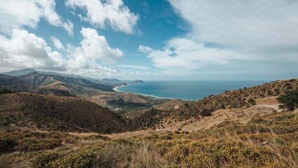 Verdant hillsides meet azure seas under a vast, bright sky in a coastal vista, presenting a scene of nature's beauty and tranquility.
