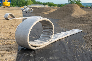 Construction photo of a roll of flat panel drainage pipe being installed on a synthetic turf multi use athletic field. 