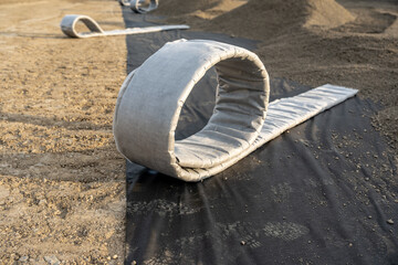 Construction photo of a roll of flat panel drainage pipe being installed on a synthetic turf multi...