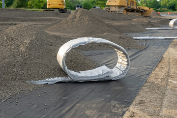 Construction photo of a roll of flat panel drainage pipe being installed on a synthetic turf multi use athletic field. 